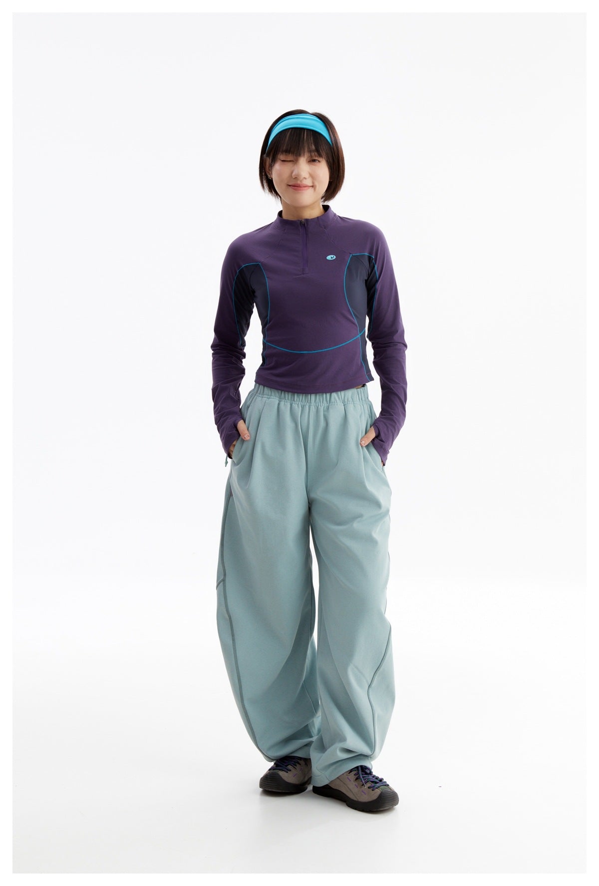 Front view of a model wearing a purple quarter-zip top with teal trim and loose pale blue pants.