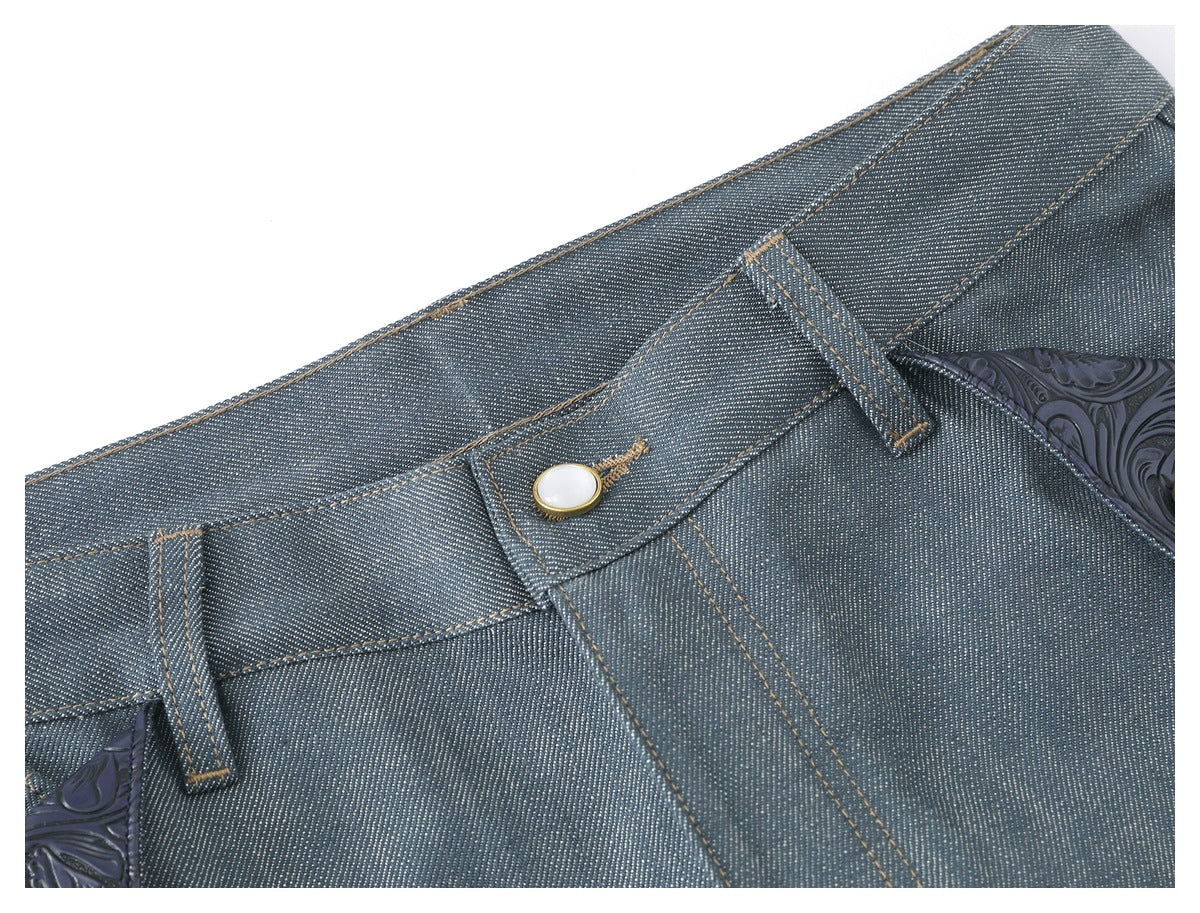 Angled close-up of blue-gray trouser waistband, belt loops, button fastening, and embossed floral trim.