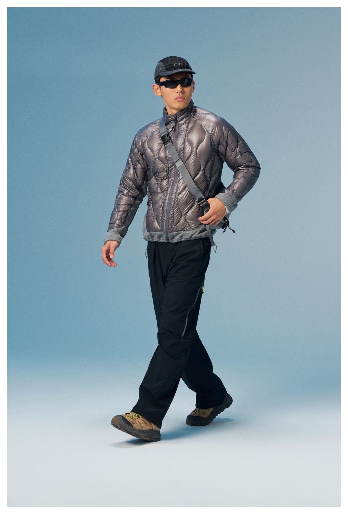 Model wearing a metallic gray quilted jacket with gray cuffs and hem, black pants, and a cap.