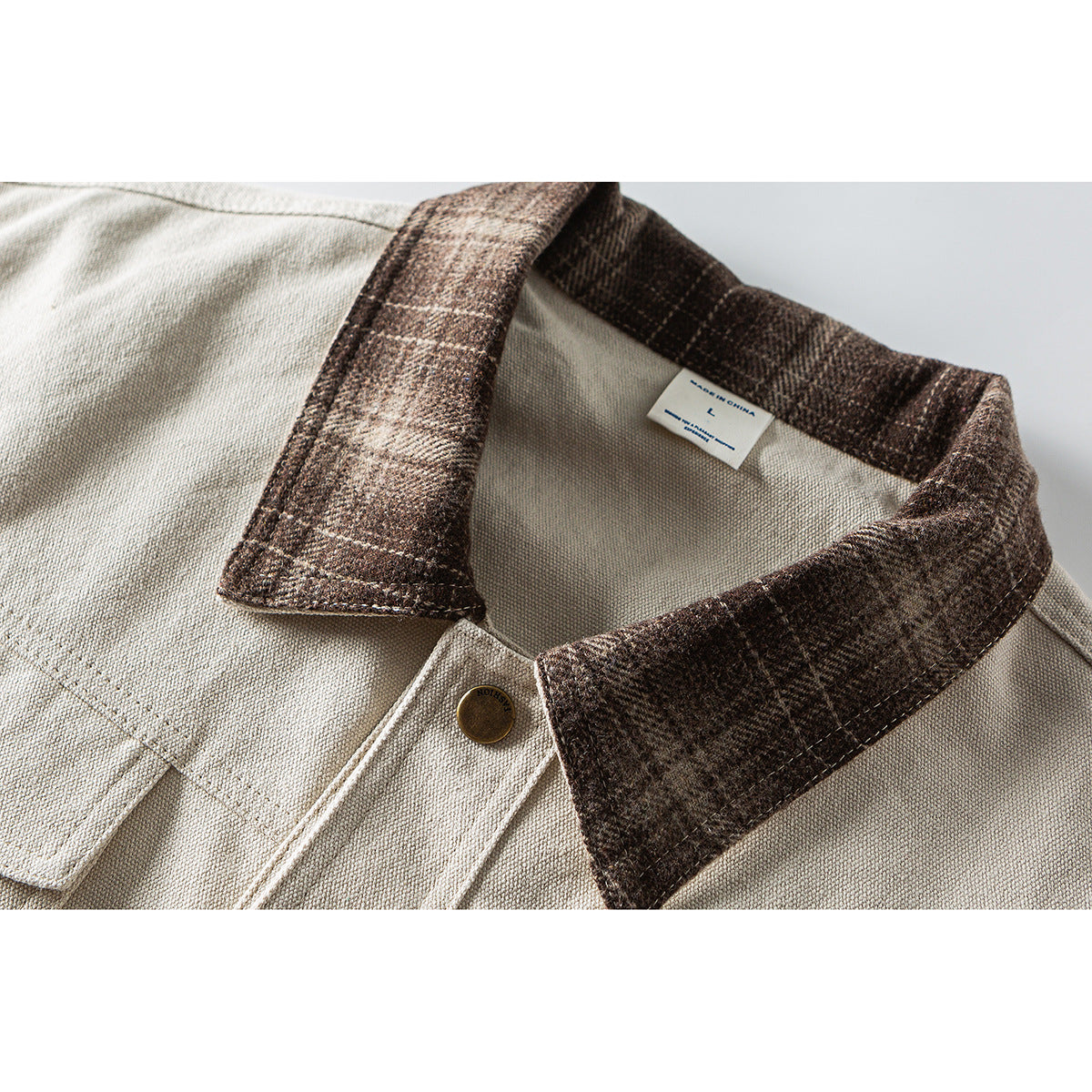 Close-up of a light beige shirt collar with a dark brown plaid collar, brass button and inner size label.