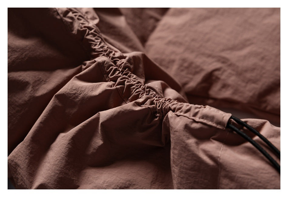 Close-up of gathered brown garment fabric with a stitched channel and black drawcords.