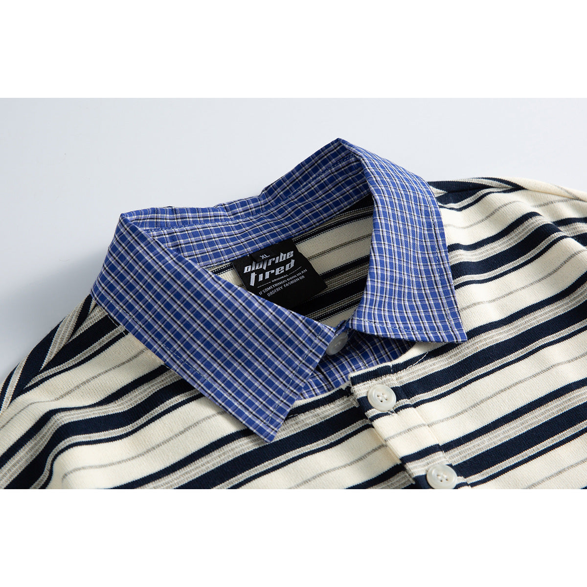 Close-up of a cream polo shirt with navy stripes, a blue plaid collar, and white buttons.
