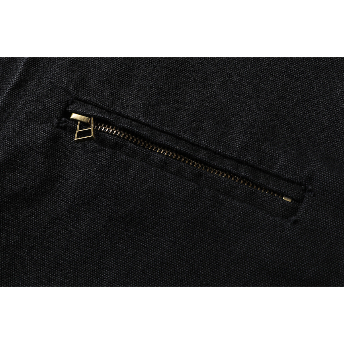 Close-up of a slanted zip pocket with a gold-tone zipper on black textured fabric.