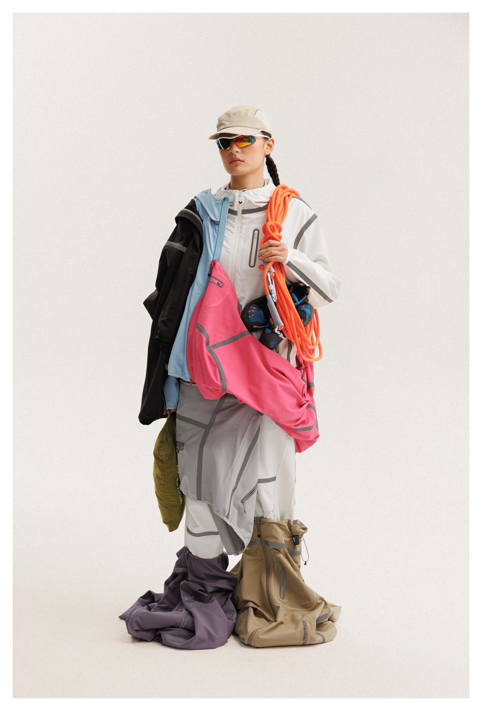 Model in a white hooded jacket and pants, carrying climbing gear and layered garments.