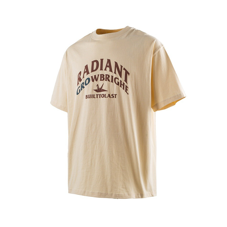 Light apricot short-sleeve crew-neck T-shirt with brown and blue arched chest graphic, angled front view