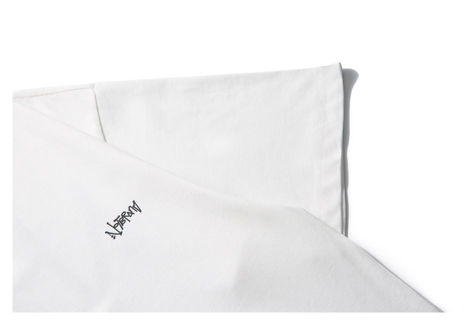 Close-up of white shirt fabric with a small black handwritten-style graphic and a folded seam.