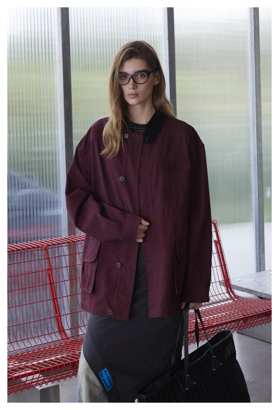 Closer view of a model wearing an oversized burgundy button-front jacket with black collar and large pockets.