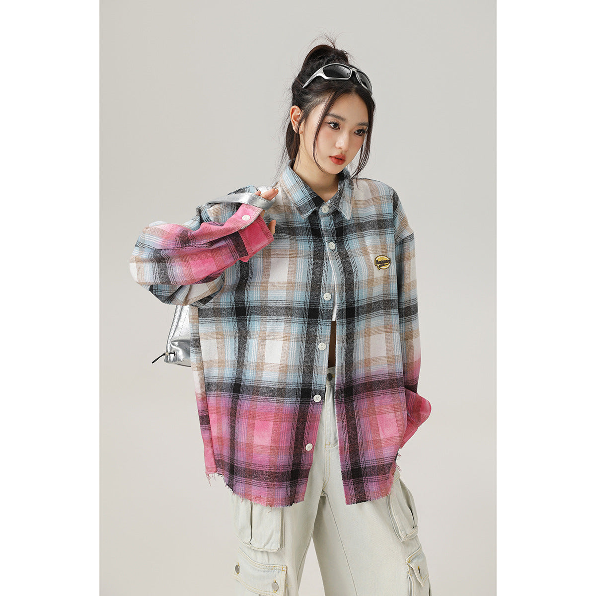 Model wearing an oversized blue, gray, and pink plaid button-up shirt with a small chest patch and light cargo pants.