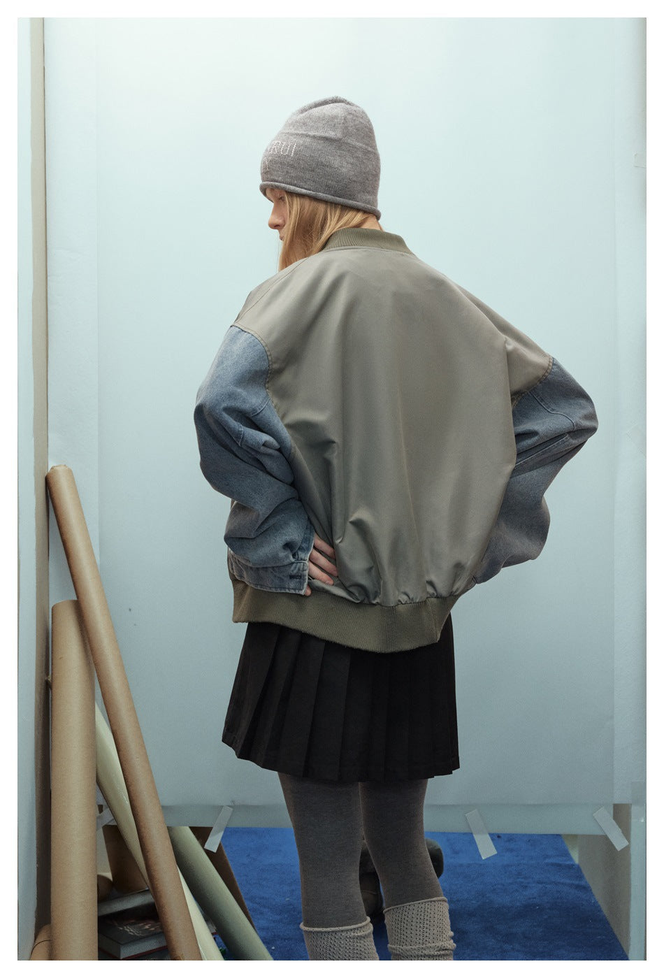 Back view of a model wearing an oversized olive-gray jacket with blue denim sleeves and a ribbed hem.