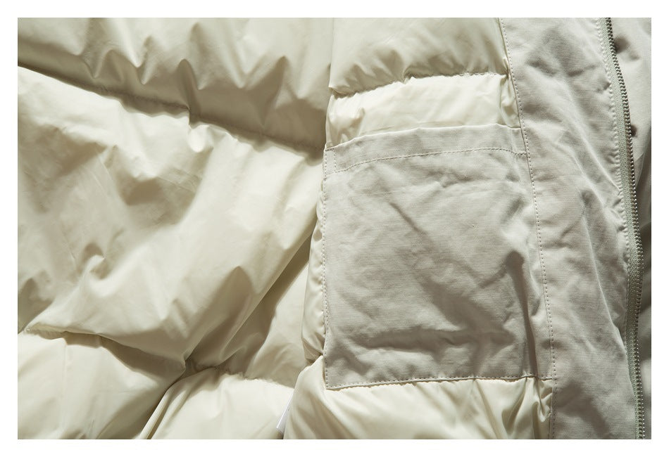 Close-up of a light cream padded jacket showing a large stitched pocket and zipper.