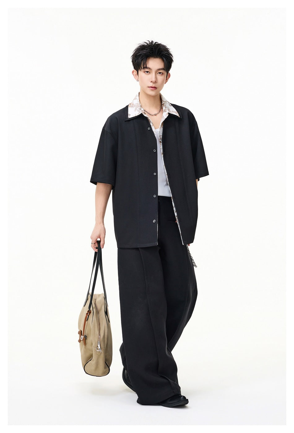 Full-length view of a model in a loose black short-sleeve button-up with a light floral collar and wide black trousers.