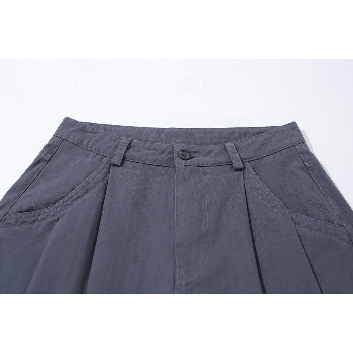Close-up of charcoal gray wide-leg trousers showing the front waistband, button, belt loops, pleats, and angled pockets.