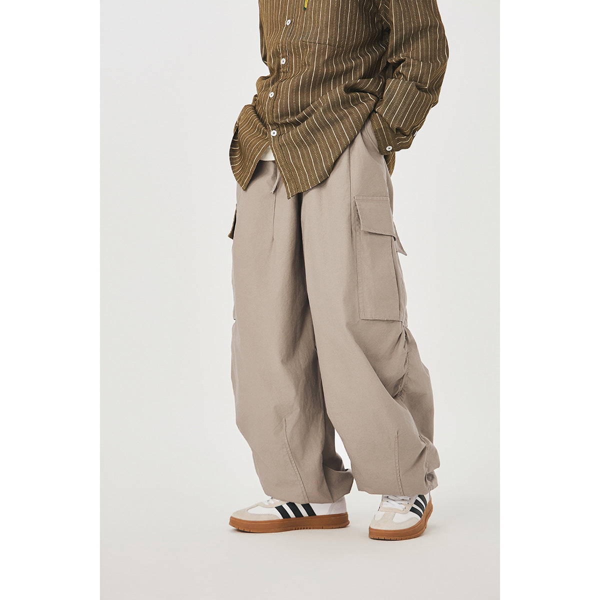 Cropped model wearing loose taupe cargo pants with a brown striped shirt and white sneakers.