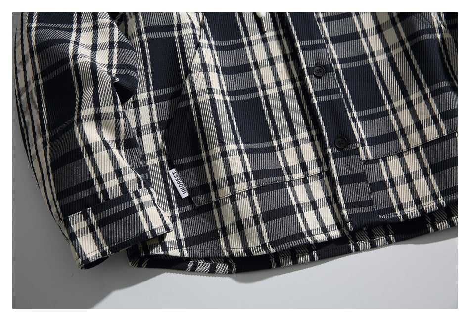 Close-up of a black, cream, and gray plaid shirt hem with black buttons and a small woven label.
