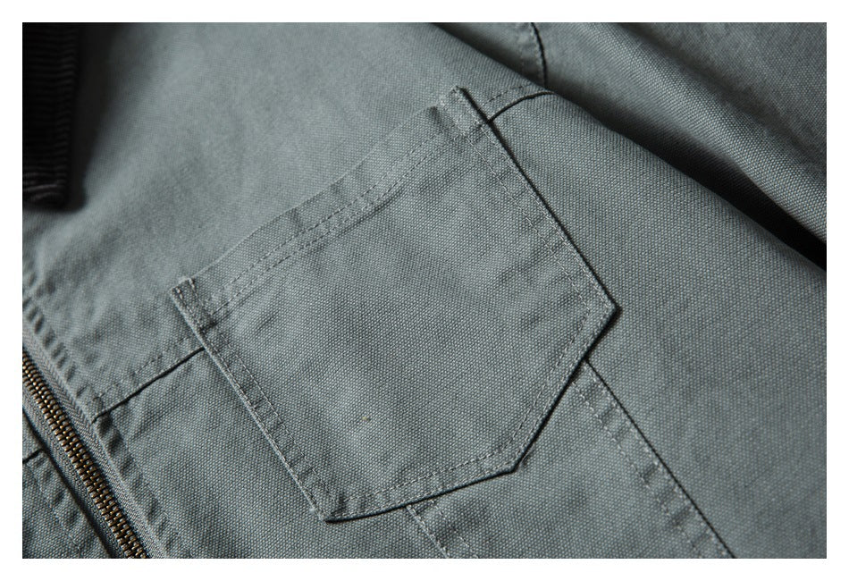 Close-up of a gray-green jacket's stitched chest pocket beside the brass-colored front zipper.