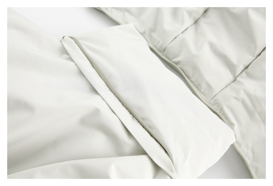 Close-up of a white jacket showing a folded fabric flap, zipper edge, and stitched seams.