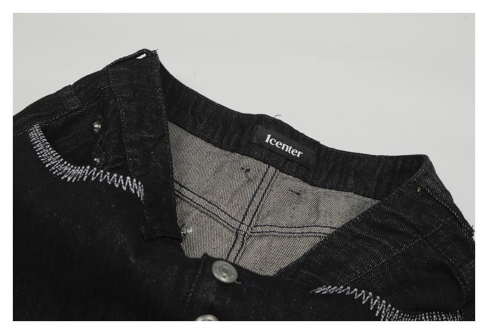 Close-up of a black denim garment showing white contrast stitching, metal buttons, and a sewn neck label.