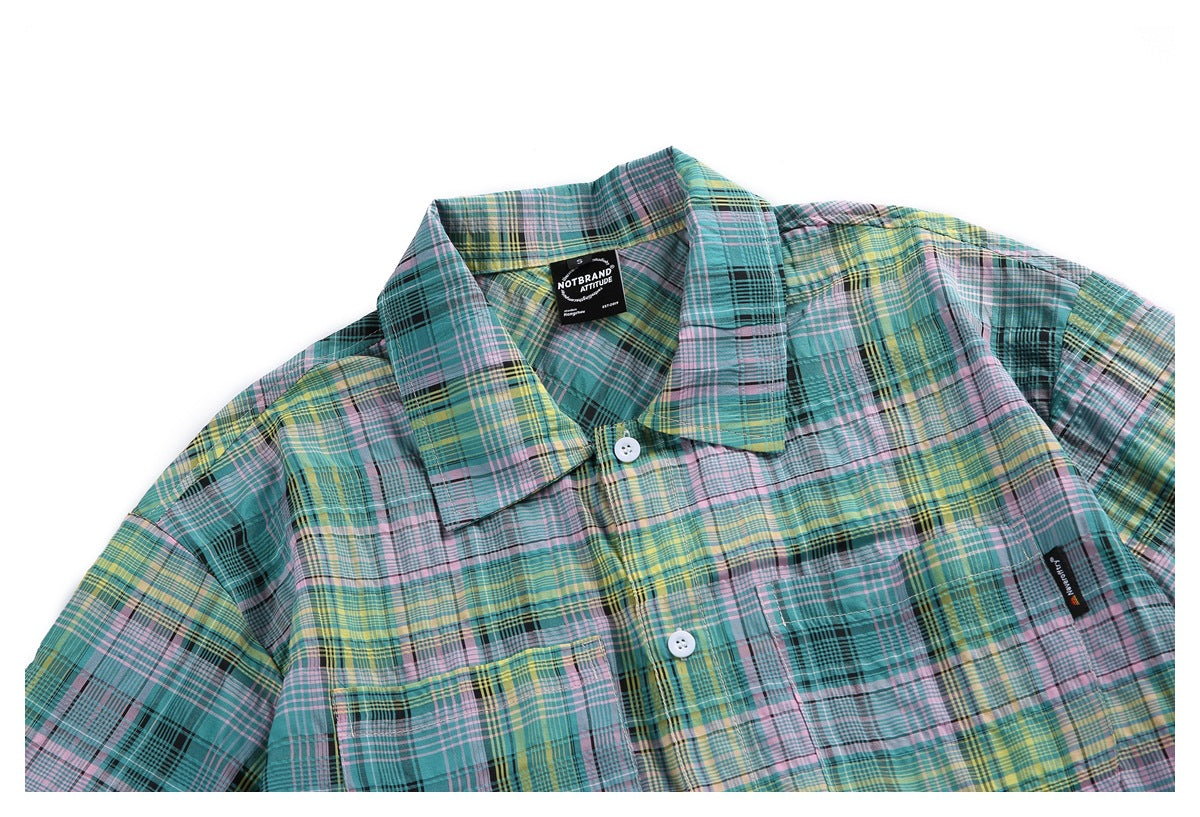 Front view of a teal, pink, yellow and black plaid button-up shirt with a collar, white buttons and chest pockets.