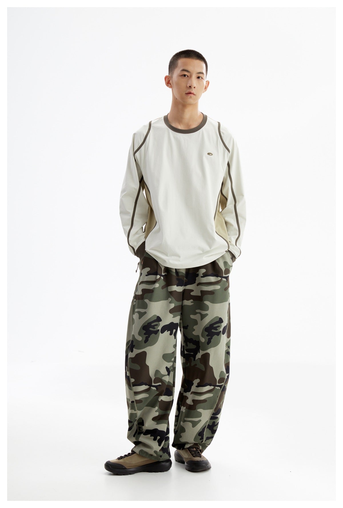 Model wearing an off-white color-block long-sleeve shirt and loose green camouflage pants, standing with hands in pockets.