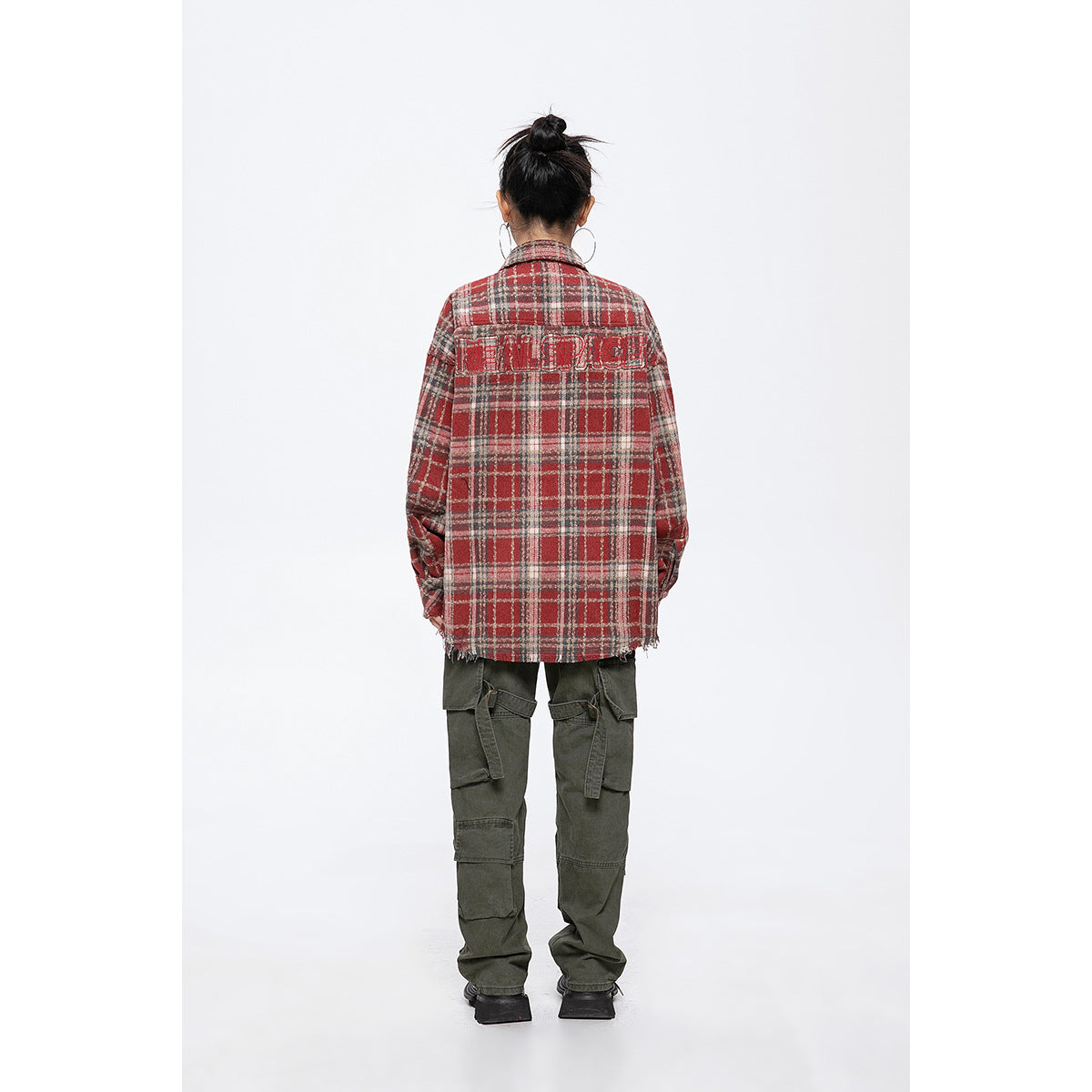Back view of a model wearing a red, gray, and cream plaid shirt jacket with a large outlined graphic across the shoulders.