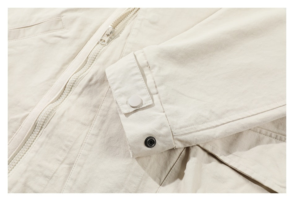 Close-up of an ivory sleeve cuff with a snap closure, beside the garment's zipper and pocket.
