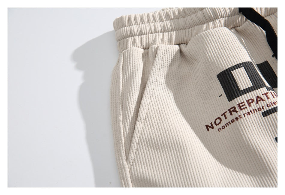 Close-up of the side pocket seam and partial lettering on ivory ribbed shorts.
