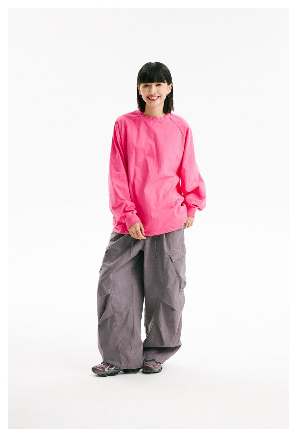 Full-length front view of a model wearing an oversized bright pink long-sleeve crewneck with gray cargo pants.