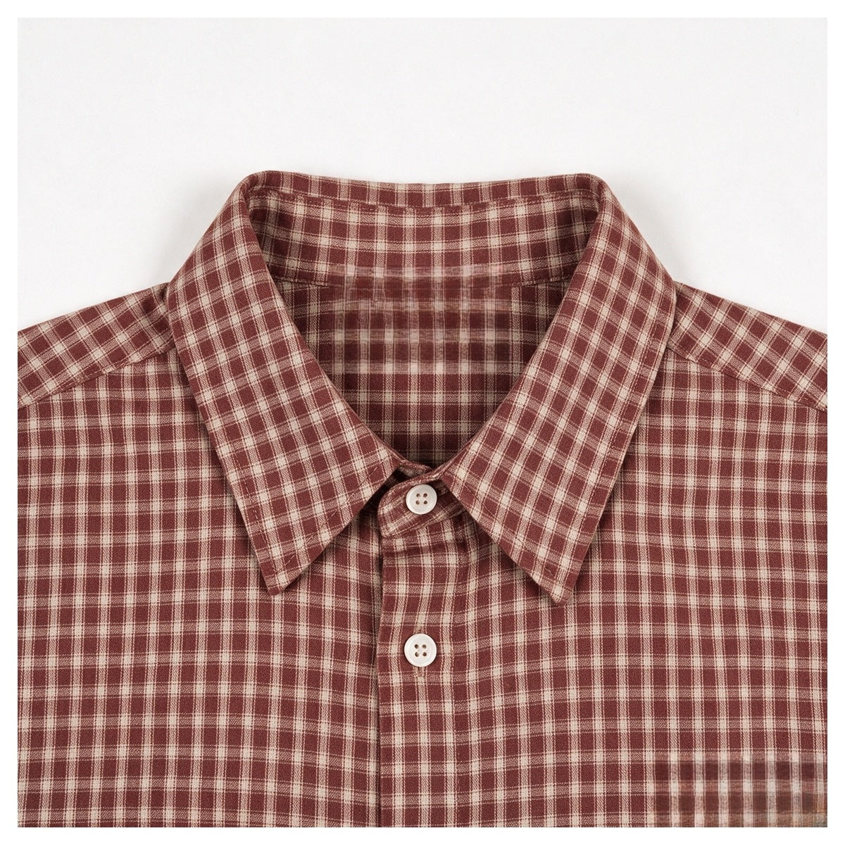 Front collar and upper chest of a rust-red and cream plaid shirt with white buttons.