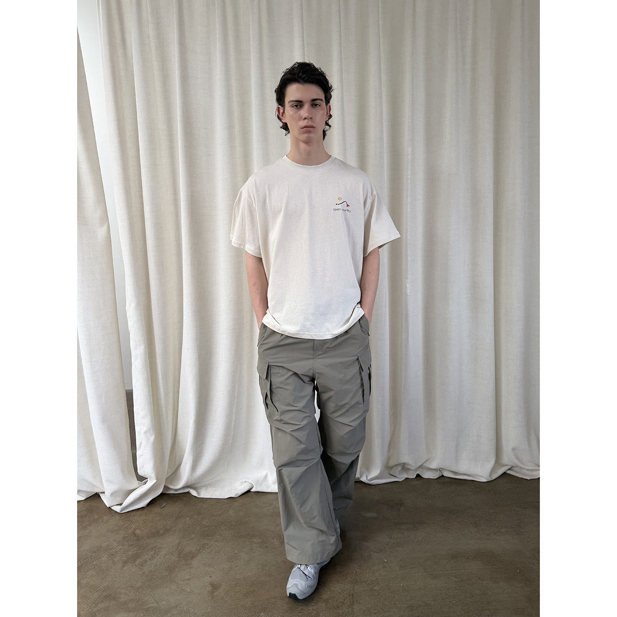 Full-length front view of a person wearing an off-white T-shirt with a small colorful chest graphic.