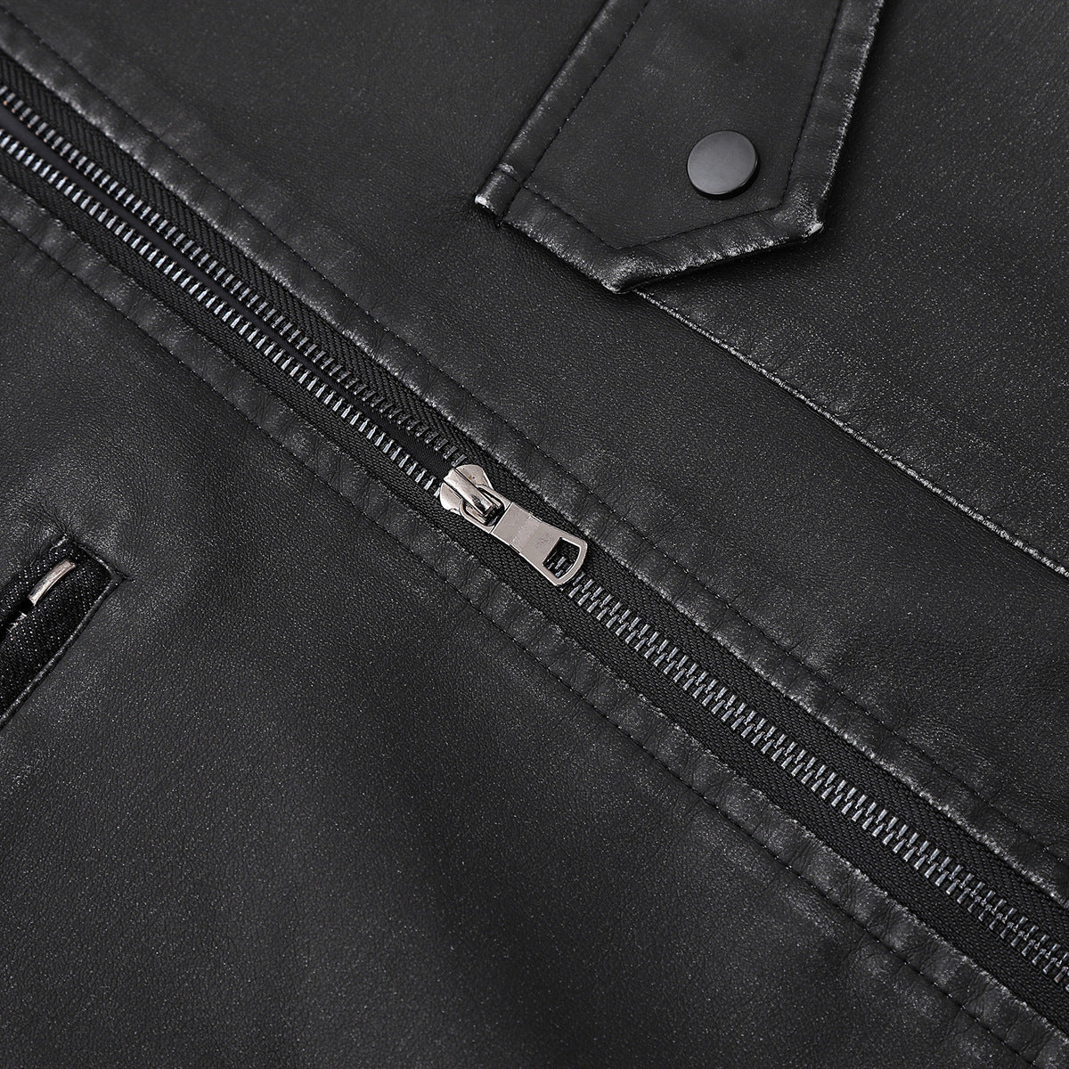 Close-up of a black jacket's diagonal zipper, silver pull, and snap-button pocket flap.
