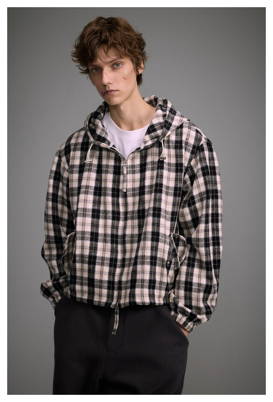 Closer view of a model wearing a pale pink, cream, and black plaid hooded jacket with a front zipper and drawcords.