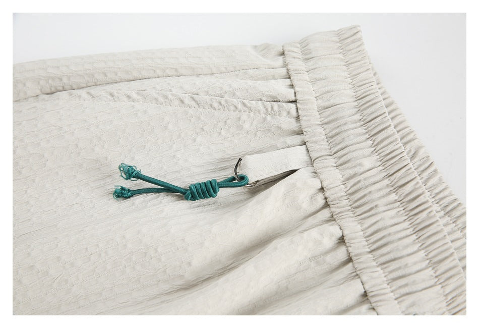 Detail of the white shorts' textured fabric, gathered waistband, and teal drawcord fastening.