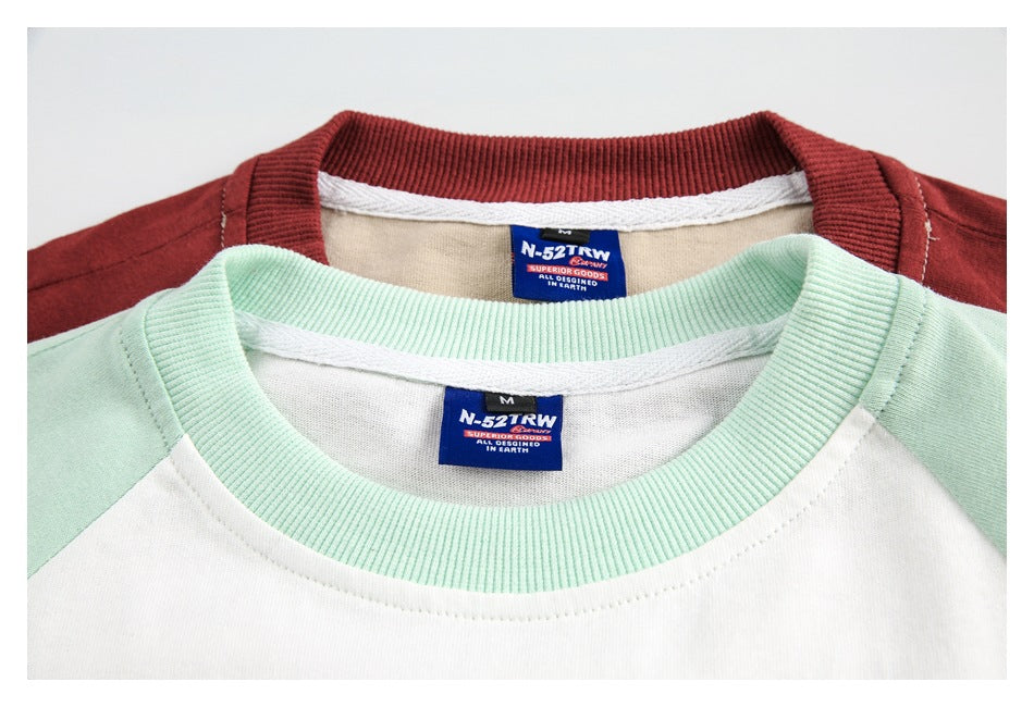 Close-up of overlapping white and beige raglan shirts with mint and burgundy ribbed collars and sewn neck labels.