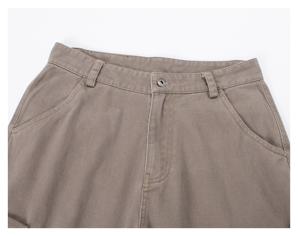 Close-up of taupe trousers showing the front waistband, button, belt loops and curved pockets.