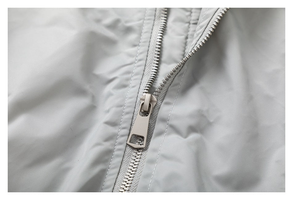Close-up of the light gray jacket's silver front zipper and stitching.