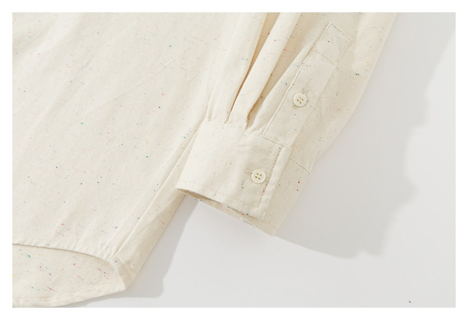 Close-up of an off-white shirt cuff with two buttons and scattered multicolor flecks.