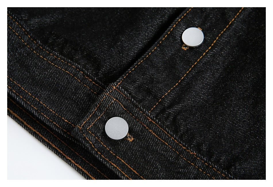 Close-up of black denim seams with orange stitching and two silver snap buttons.