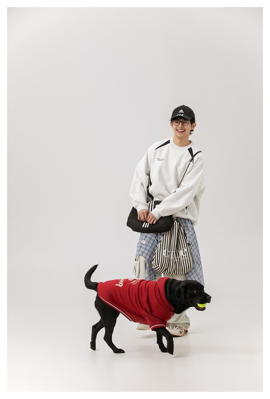 Model wearing a light gray sweatshirt with black panels, standing behind a dog in a red coat.