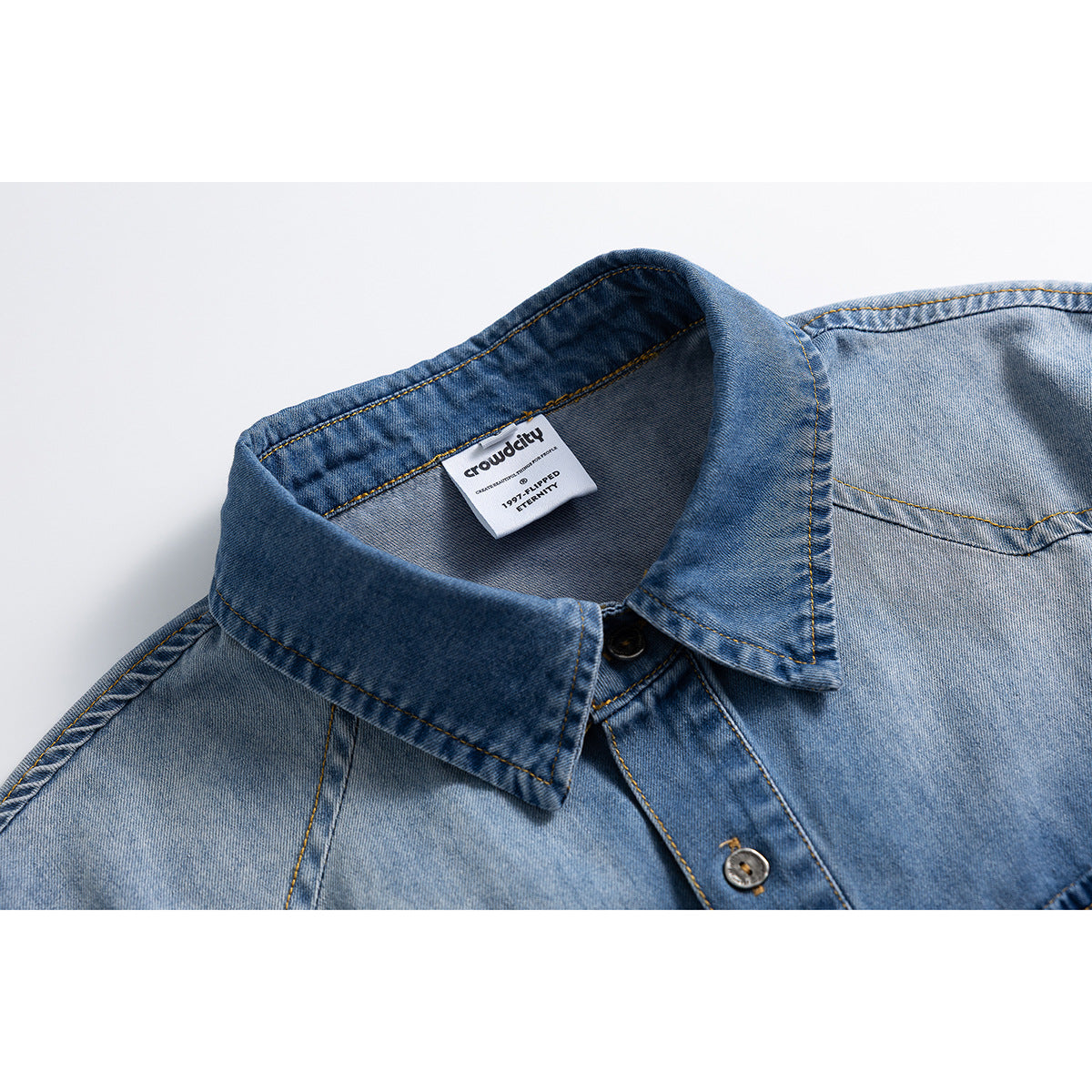 Close-up of a light blue denim shirt collar, button placket, contrast stitching and interior neck label.