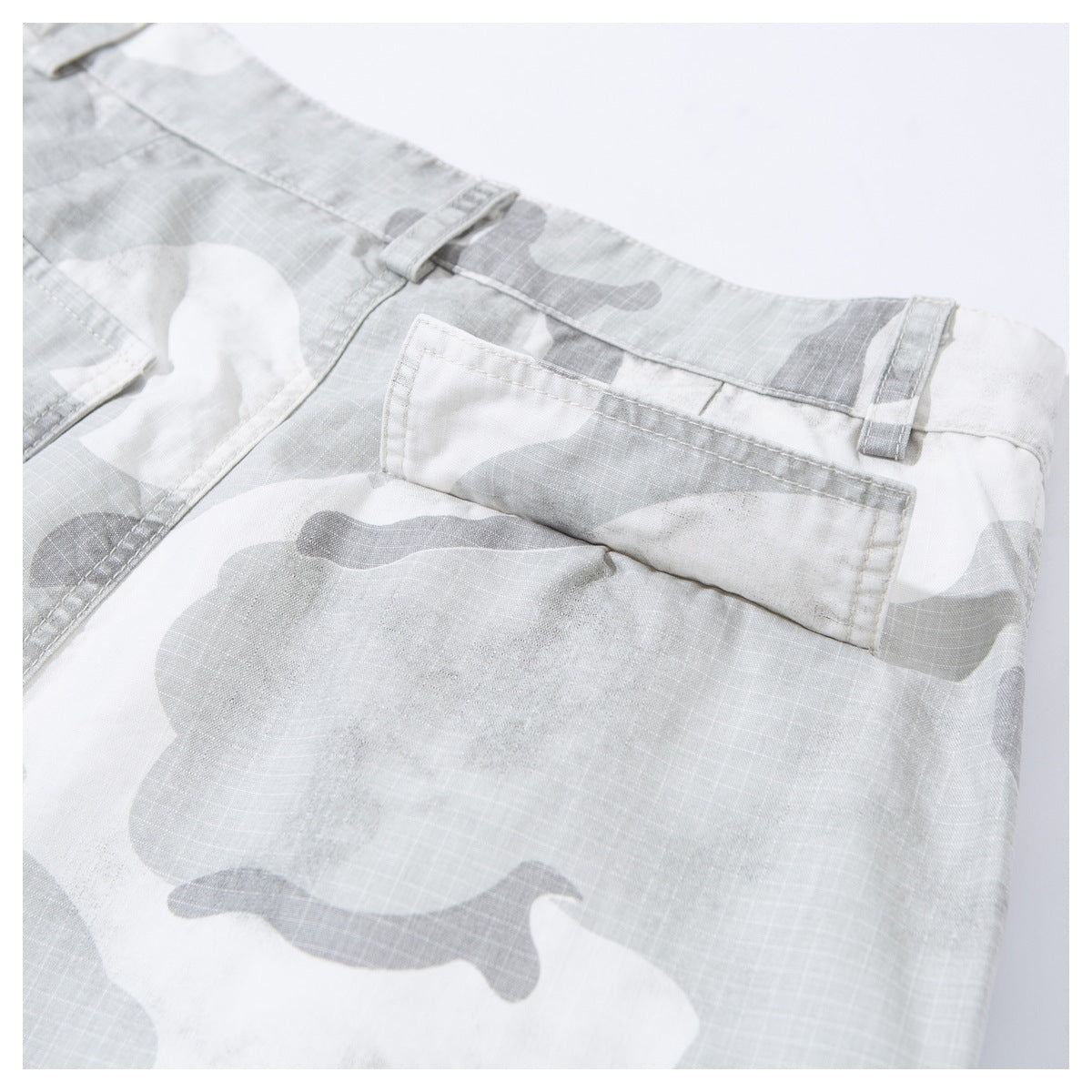 Close-up of a rear pocket and belt loops on gray and white camouflage shorts.
