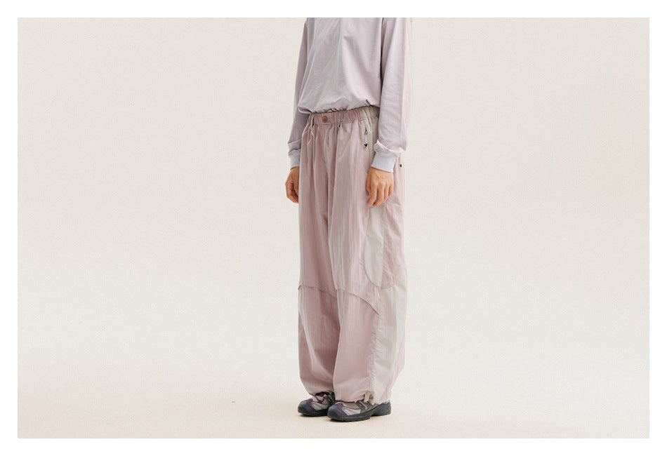 Model wearing loose pale mauve pants with an elastic waist and curved panel seams, shown from the front at an angle.