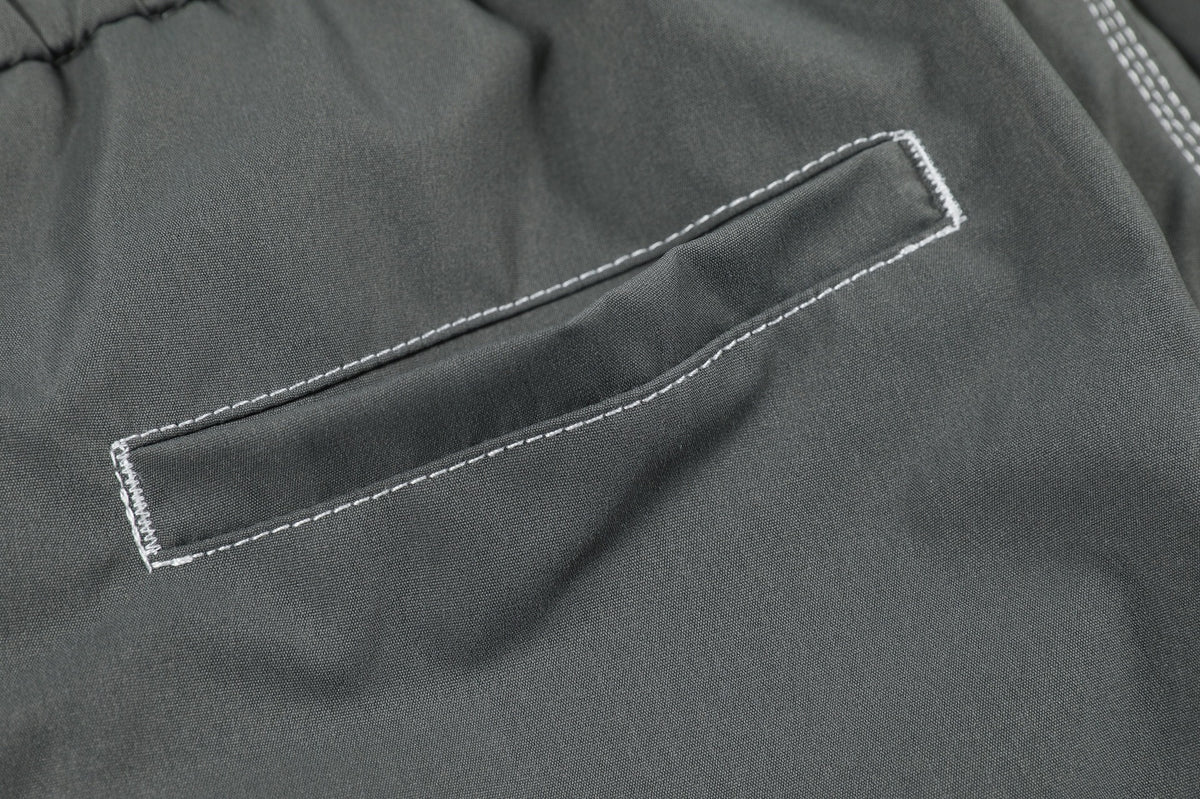 Close-up of a charcoal gray garment pocket flap outlined with contrasting white stitching.