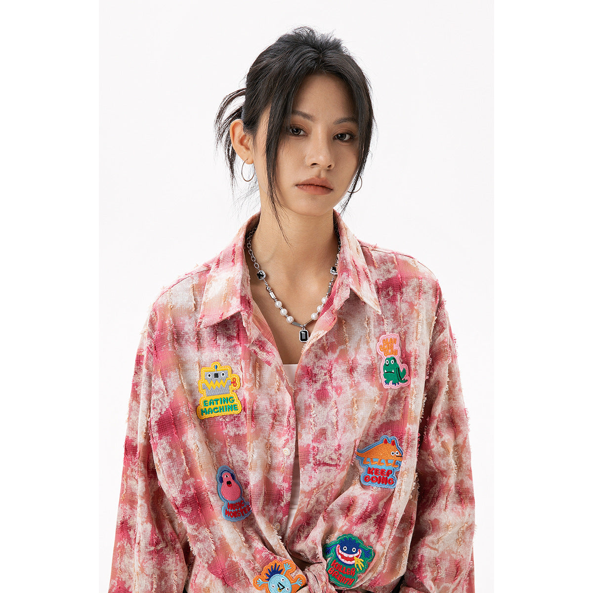 Close view of a model wearing a pink marbled shirt with colorful cartoon patches and a pointed collar.