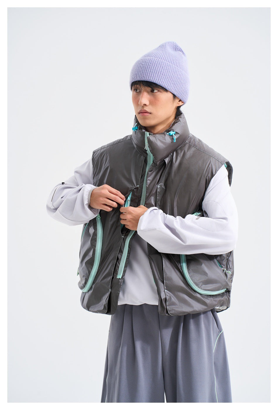 Model demonstrating the front zipper and large turquoise-trimmed pockets on a charcoal-gray vest.