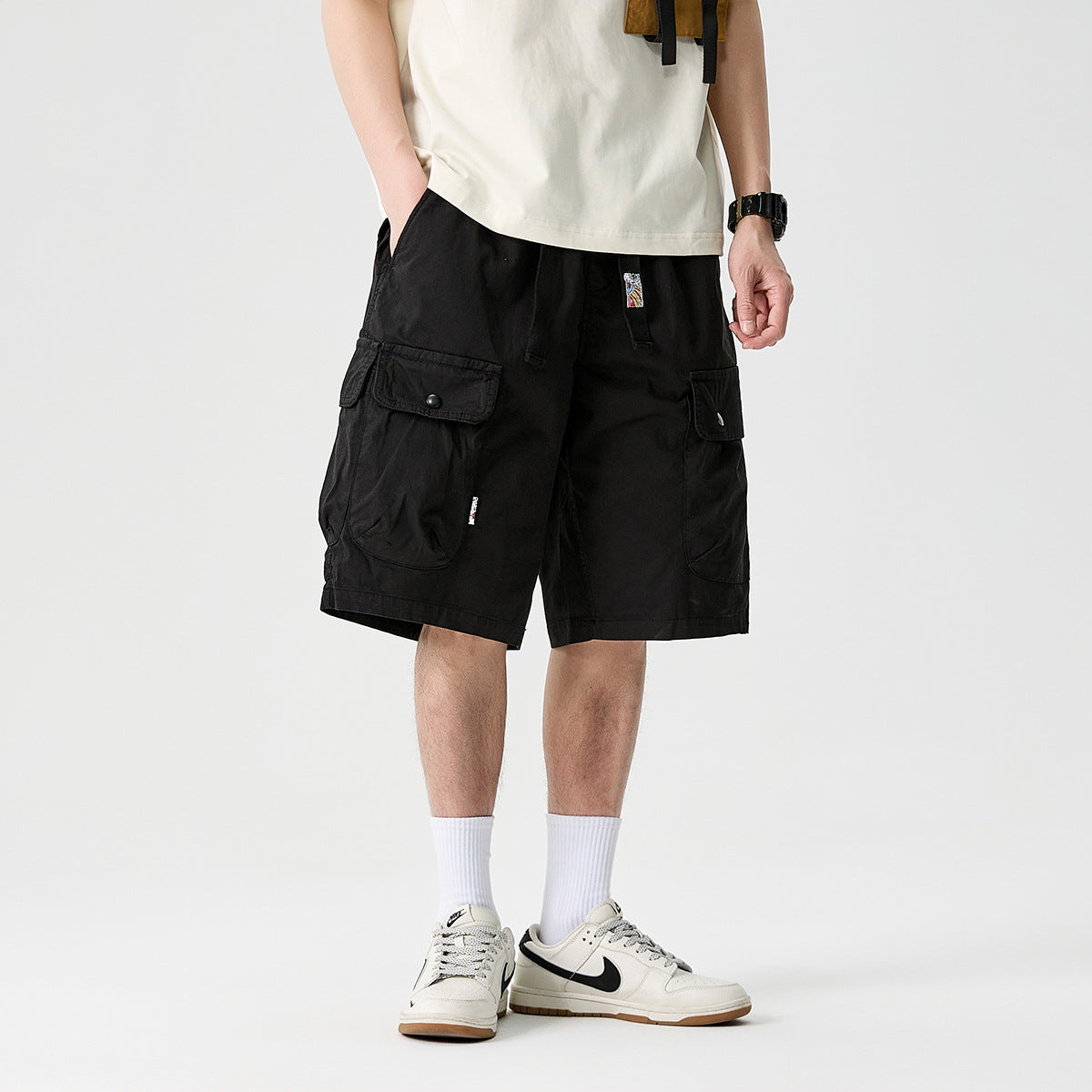 Cropped model wearing black knee-length cargo shorts with large flap pockets and a white T-shirt.