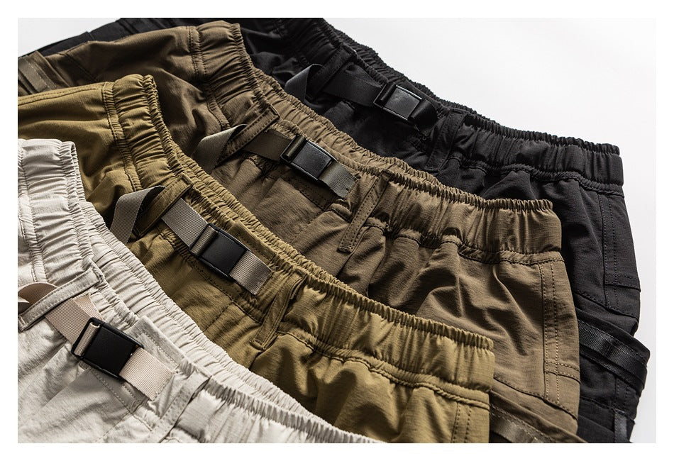 Close-up of cargo shorts in light beige, olive-brown and black, showing elastic waists and adjustable buckle straps.