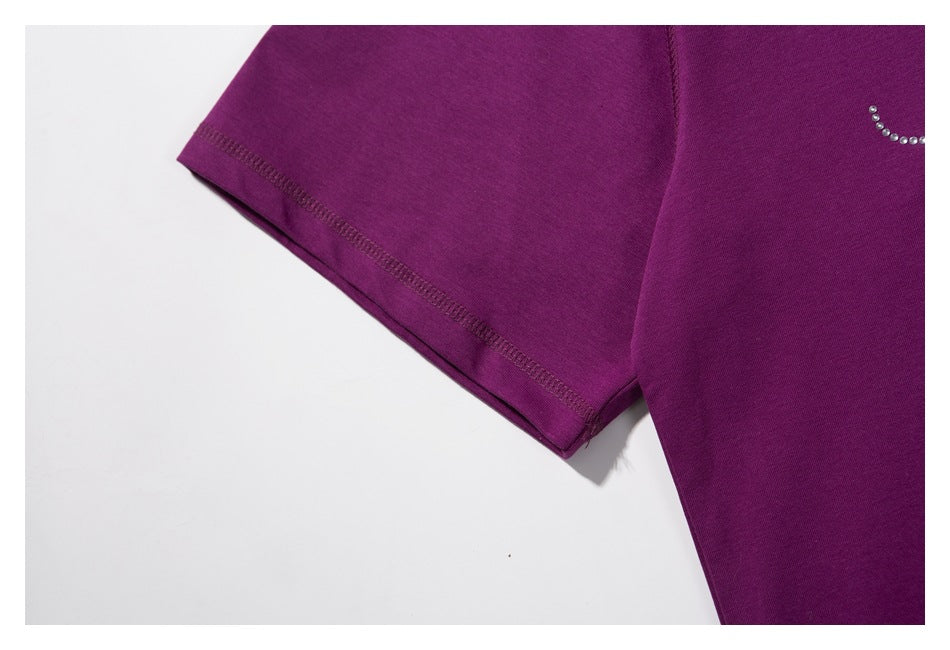 Close-up of a purple shirt sleeve and seam, with part of a curved rhinestone embellishment visible.