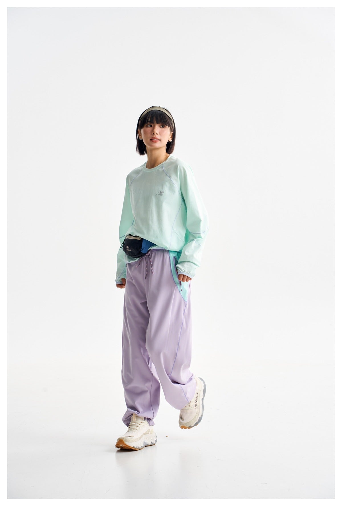 A woman models a mint long-sleeve top and loose lavender trousers in a three-quarter pose against white.