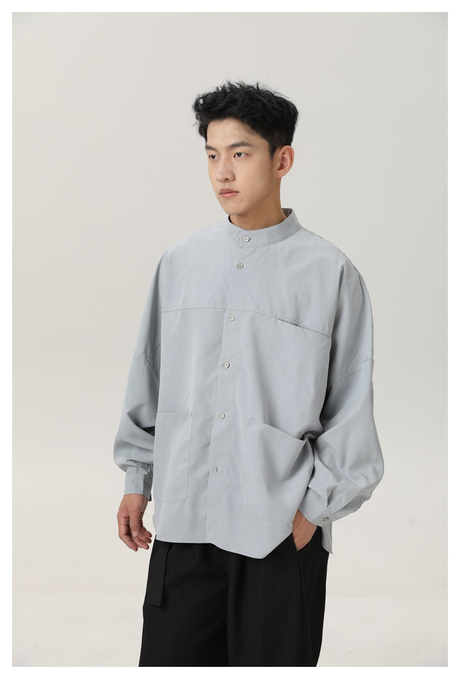 Three-quarter view of a model wearing a light gray oversized button shirt with stand collar and two large front patch