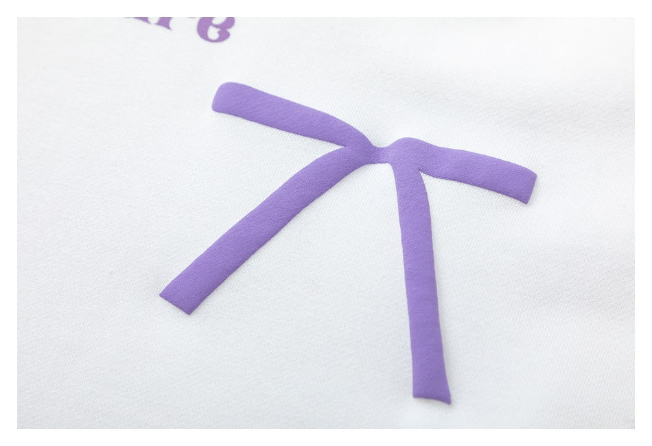 Close-up of a raised purple bow graphic on the white hoodie.